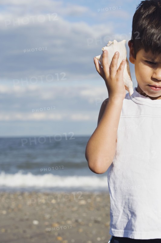 Young Hispanic boy listening to seashell