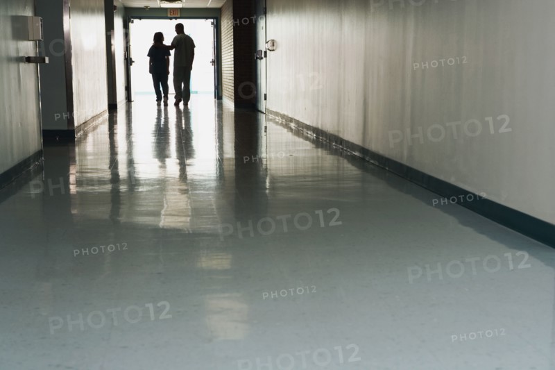 Two people standing at end of corridor in hospital