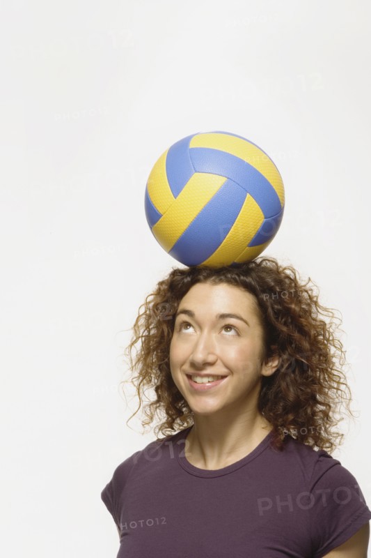 Mixed Race woman balancing volleyball on head