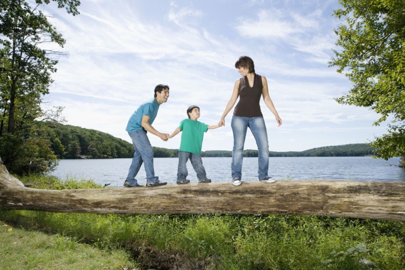 Parents helping son walk across log