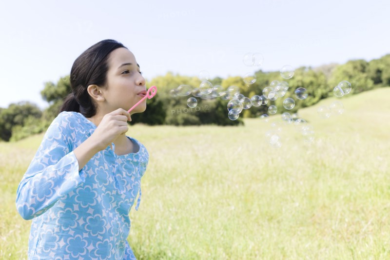 Hispanic girl blowing bubbles in field