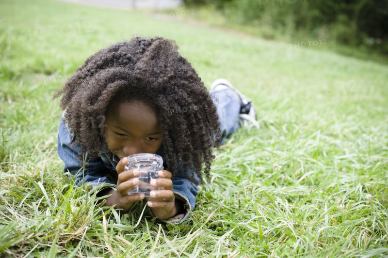 African American boy laying in grass and looking in jar