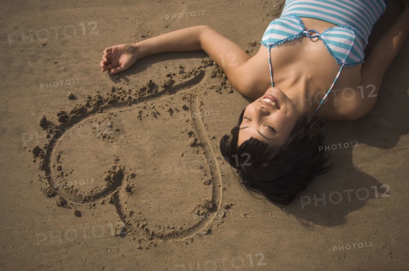 Asian woman laying next to heart in sand