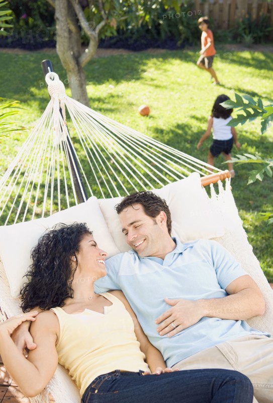 Couple in hammock with children playing in background