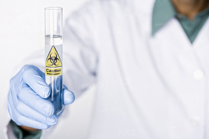 Hispanic scientist holding test tube with caution sticker full of water