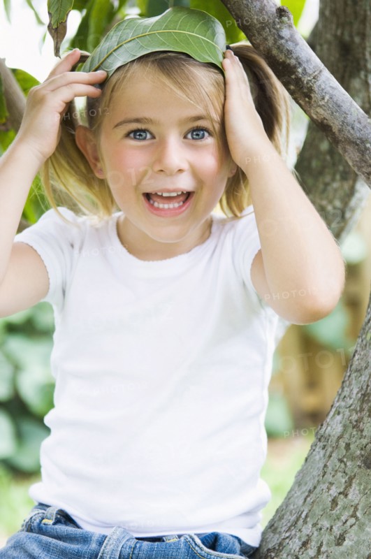 Caucasian girl sitting in tree holding leaf in hair