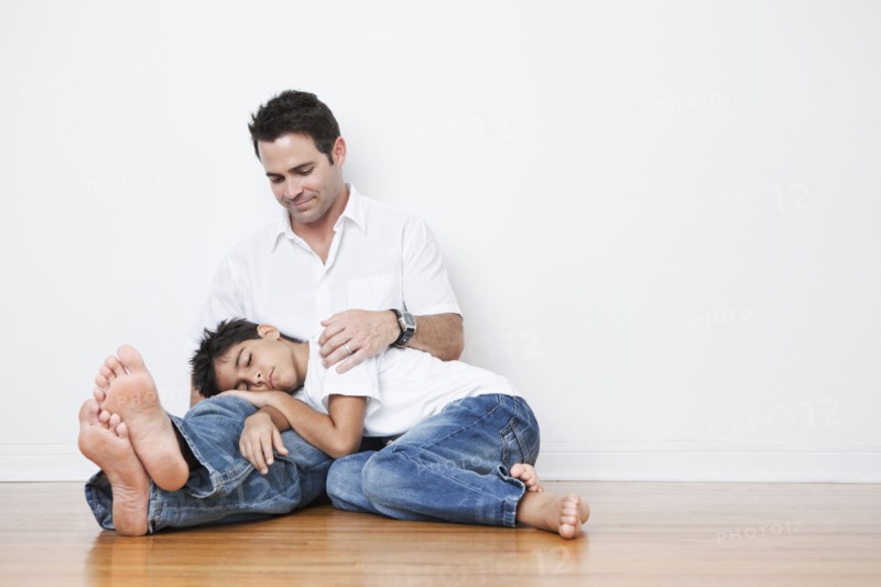 Mixed Race boy napping in lap of father on floor