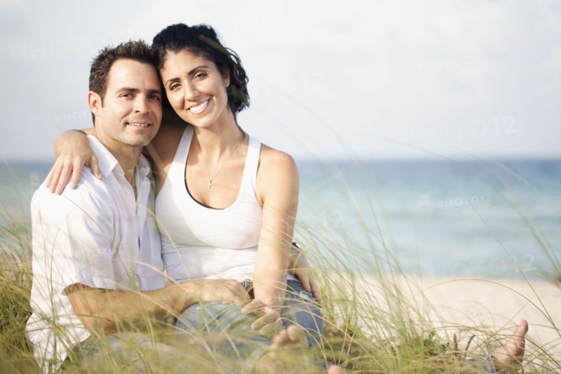 Portrait of Mixed Race couple sitting in grass at beach