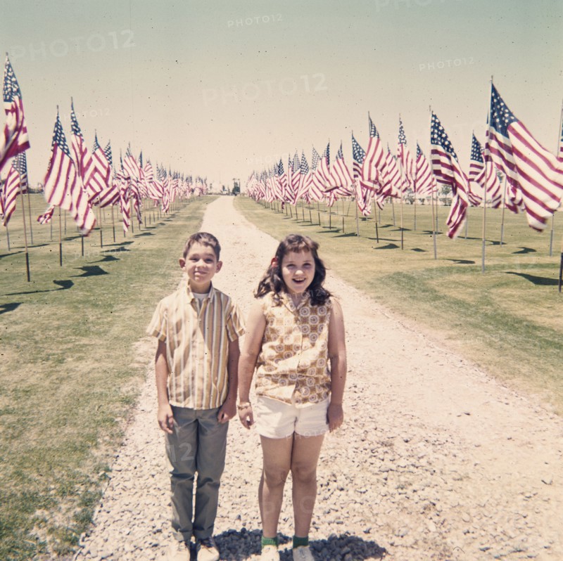 Caucasian brother and sister holding hands near American flags