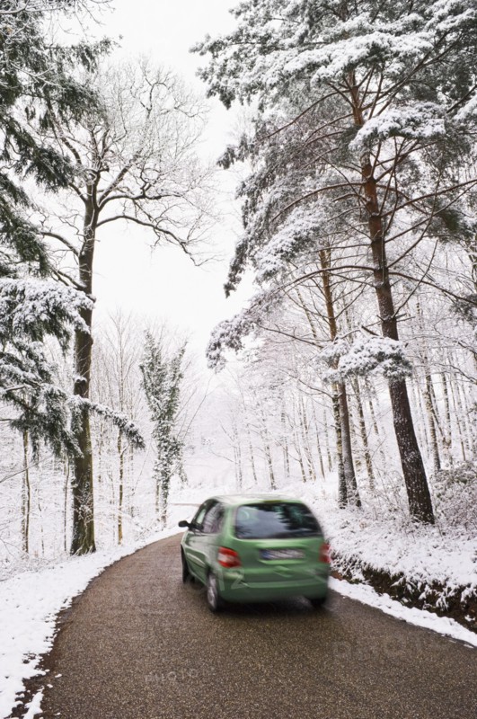 Green car driving on narrow road in winter