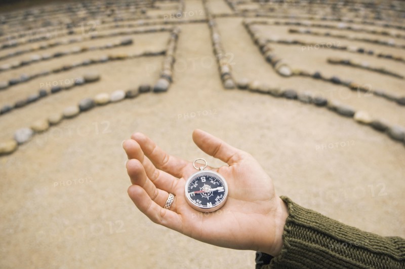 Hand of Mixed Race woman holding compass in maze