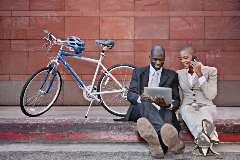 Business people sitting on curb using digital tablet and cell phone