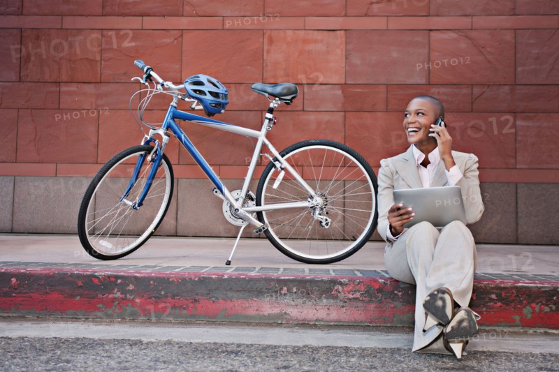 Businesswoman sitting on curb using digital tablet and cell phone