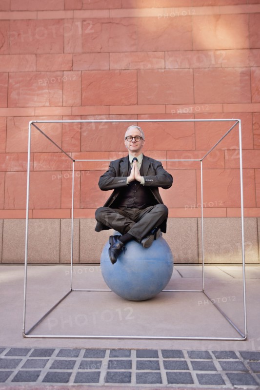 Caucasian businessman practicing yoga on ball inside of box