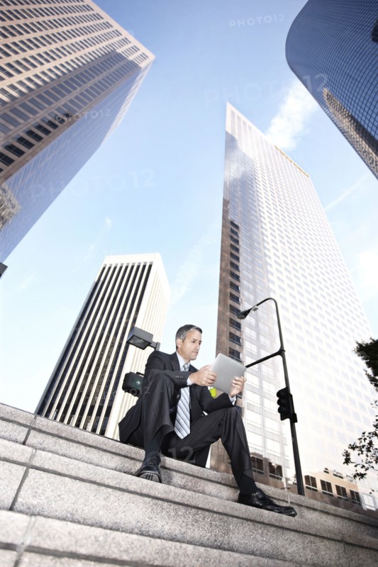 Hispanic businessman sitting on steps with digital tablet