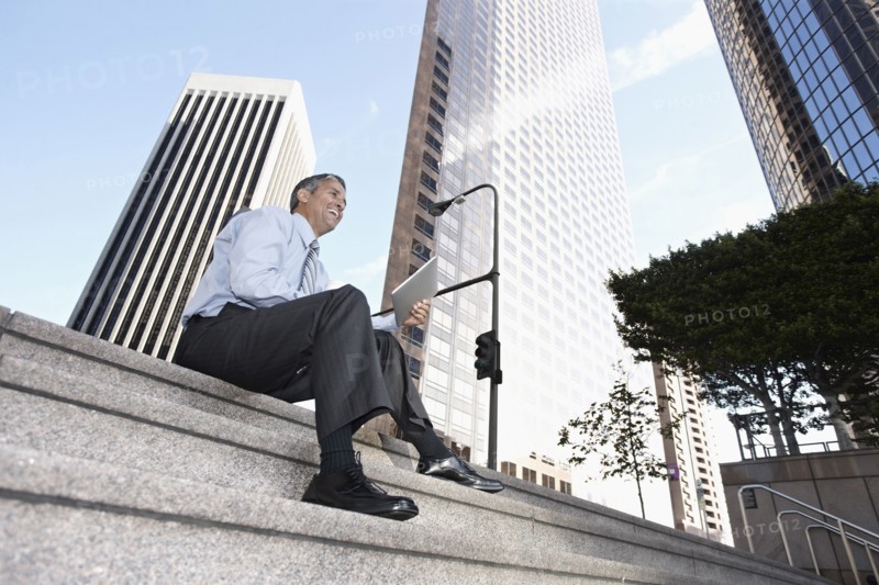 Hispanic businessman sitting on steps with digital tablet