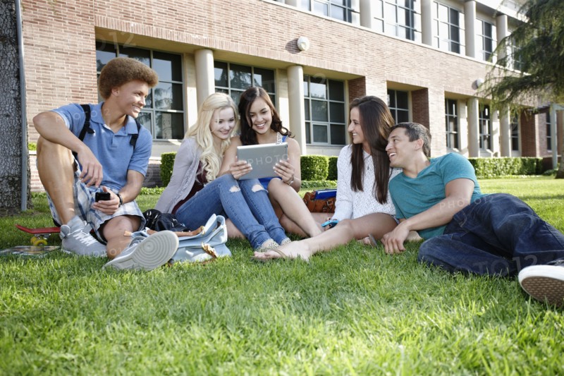 School friends hanging out on grass with digital tablet