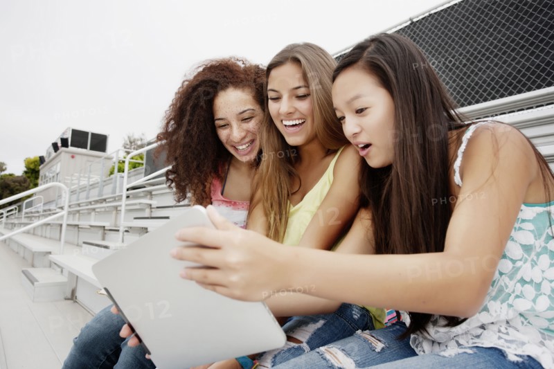 School friends sitting together on bleachers using digital tablet