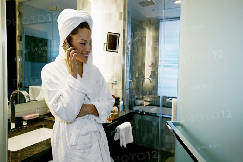 Mixed race woman talking on cell phone in bathroom