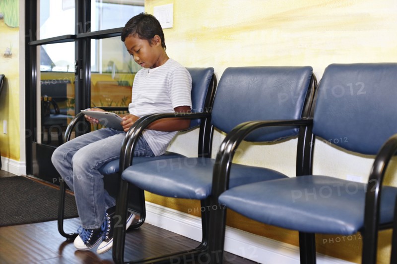Mixed race boy using digital tablet in waiting room