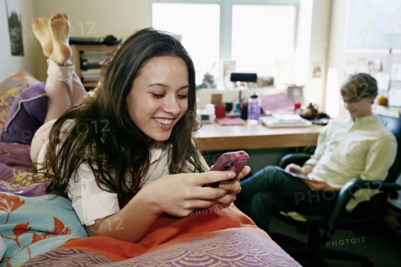 Mixed race college student using cell phone in dorm