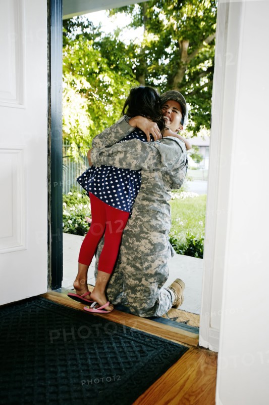 Mixed race soldier mother hugging daughter in front door
