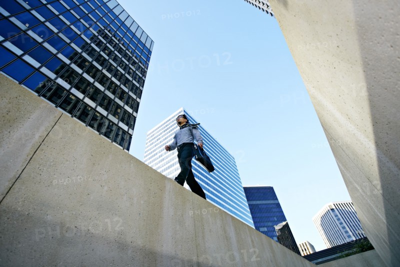 Asian businessman walking on ledge in city