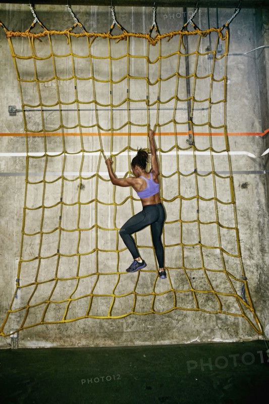 African American woman climbing net wall in gym