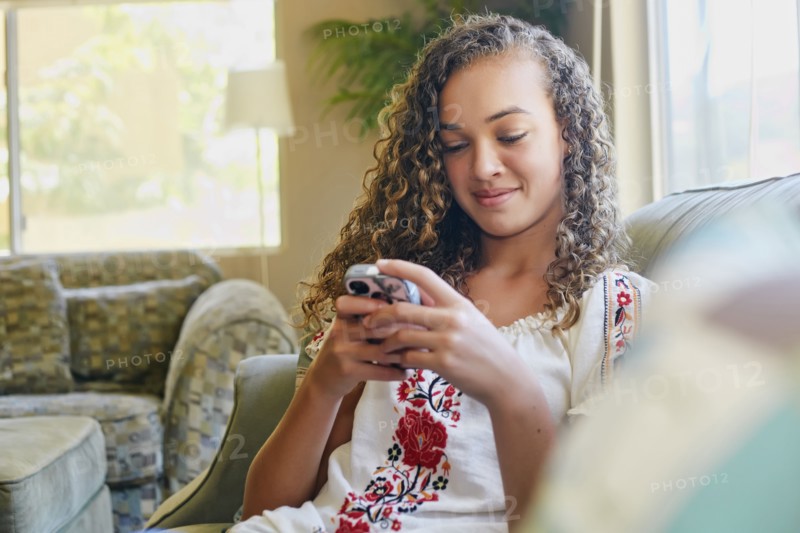 Mixed race girl using cell phone on sofa