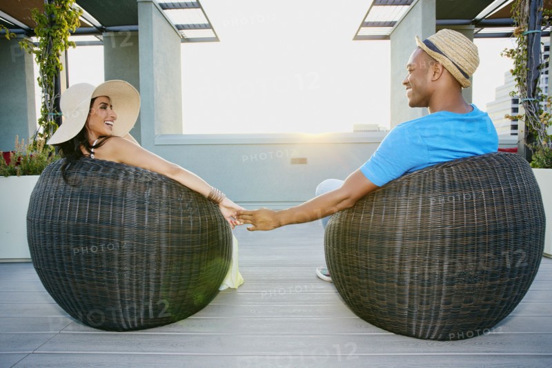 Couple holding hands in wicker chairs on balcony