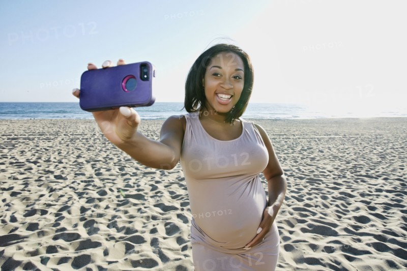 Pregnant woman taking cell phone picture on beach