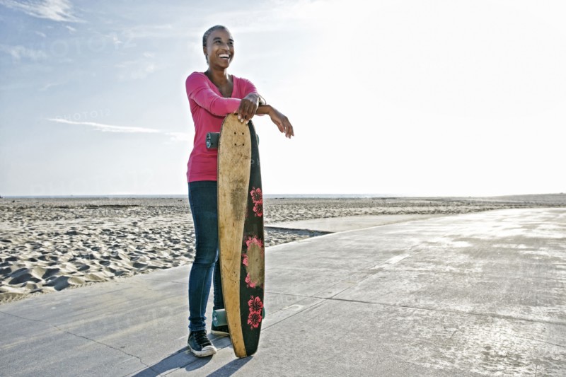 Older Black woman holding skateboard on beach