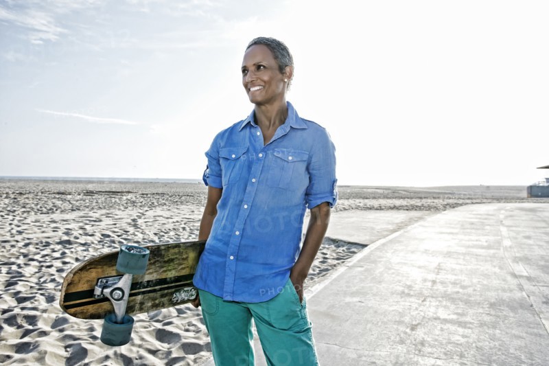 Older Black woman holding skateboard on beach