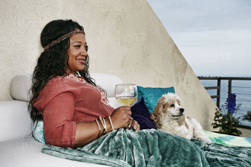 Mixed race woman drinking wine at waterfront with dog
