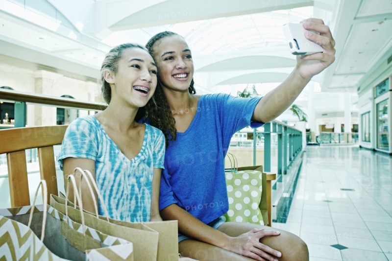 Mixed race teenage girls taking cell phone photograph at shopping mall