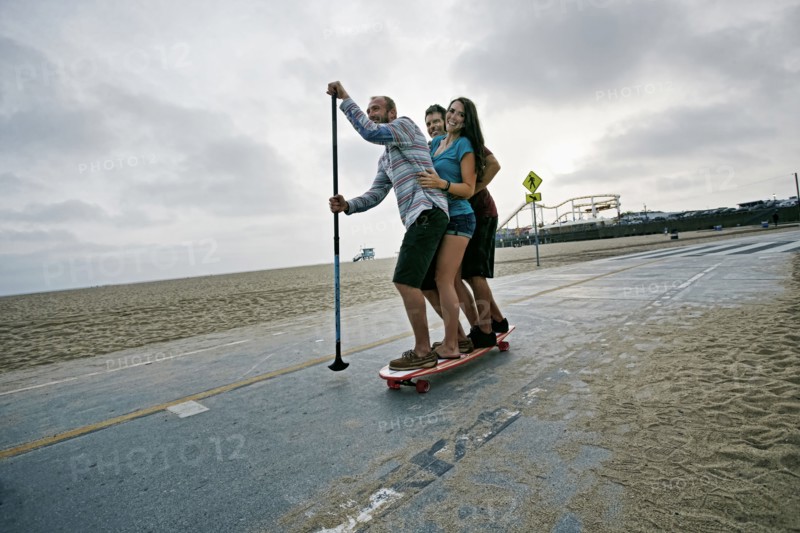 Friends skateboarding with paddle pole at beach
