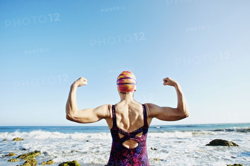 Older Caucasian woman flexing her muscles on beach