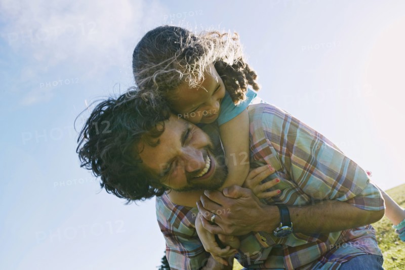 Low angle view of father carrying daughter piggyback outdoors