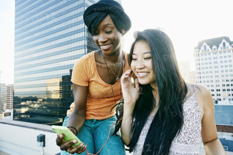 Women listening to earbuds on urban rooftop