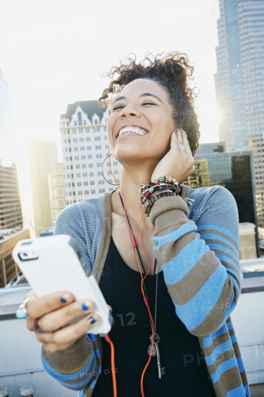 Mixed race woman listening to earbuds on urban rooftop