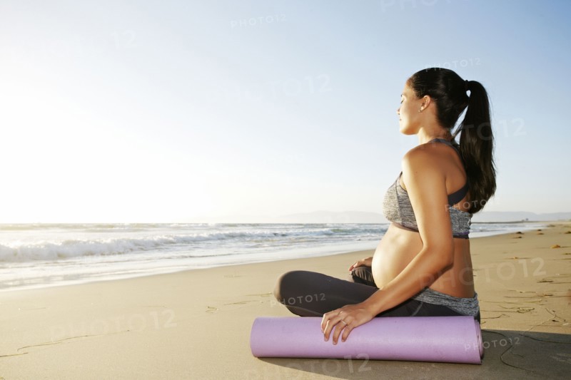 Pregnant Hispanic woman meditating on beach