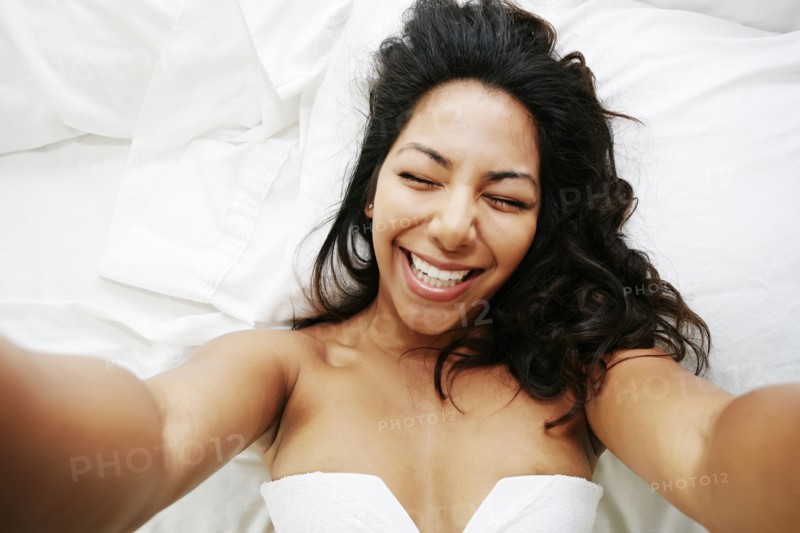 Hispanic woman taking selfie of herself on bed
