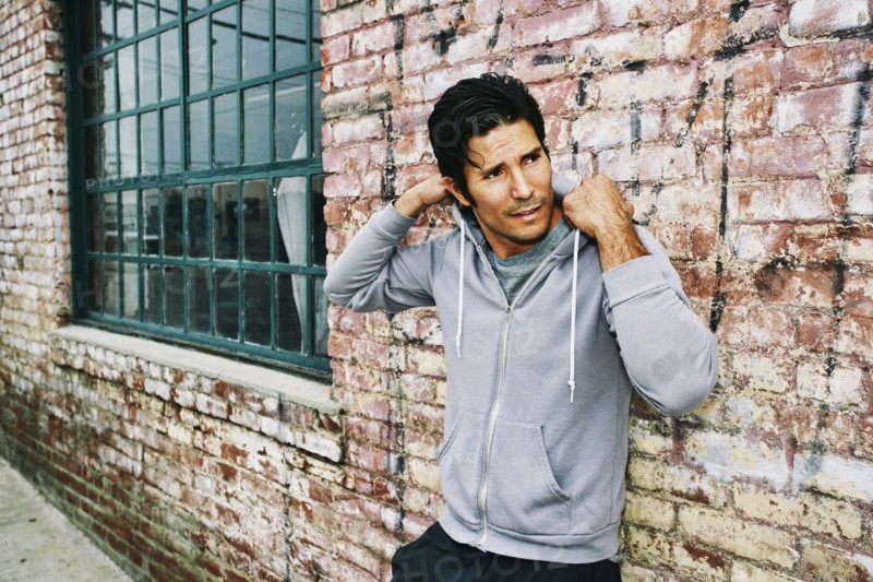 Mixed race man leaning on brick building