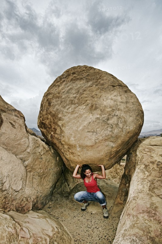 Hispanic woman lifting boulder on rocky hillside