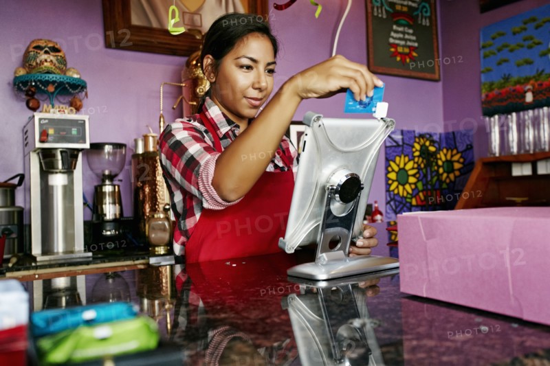Hispanic barista using digital tablet register in coffee shop