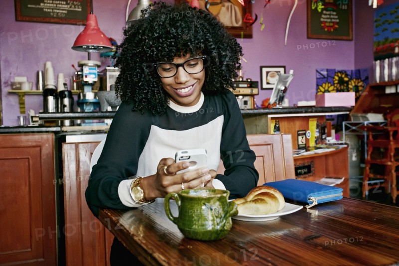 Mixed race woman using cell phone in cafe