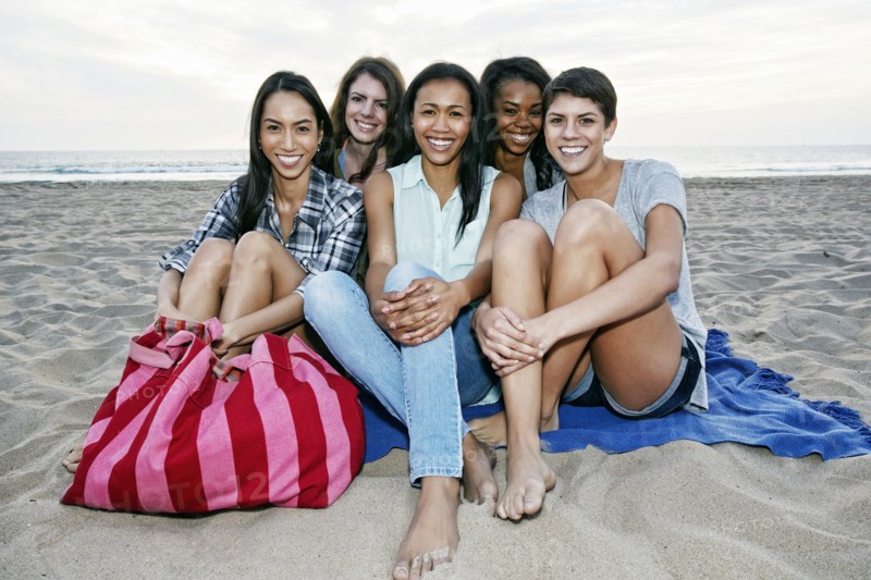Smiling women sitting on blanket on beach