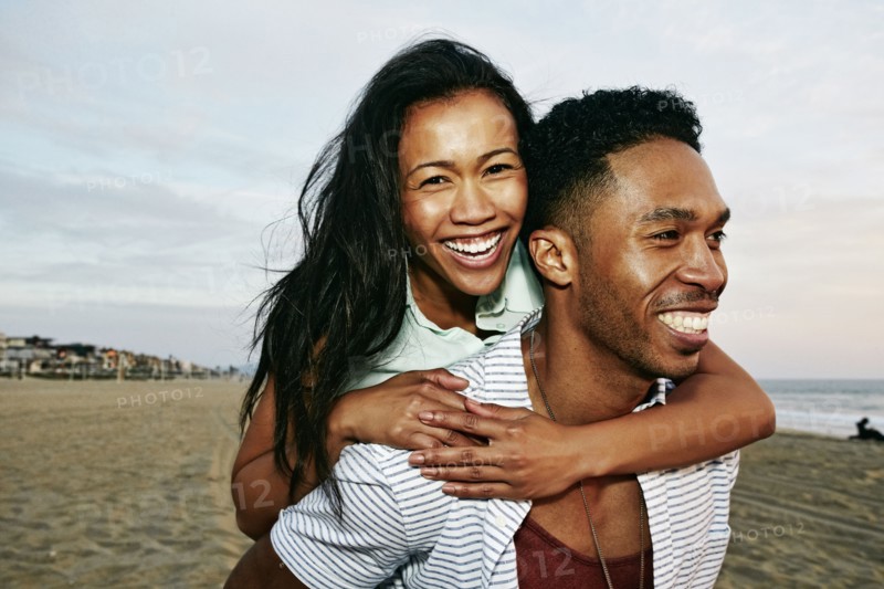 Man carrying girlfriend piggyback on beach