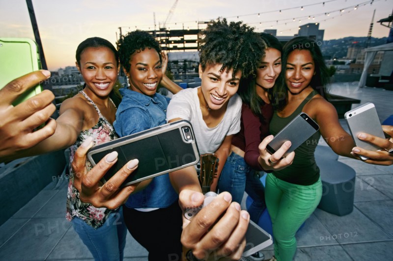 Women taking selfies with cell phones on urban rooftop