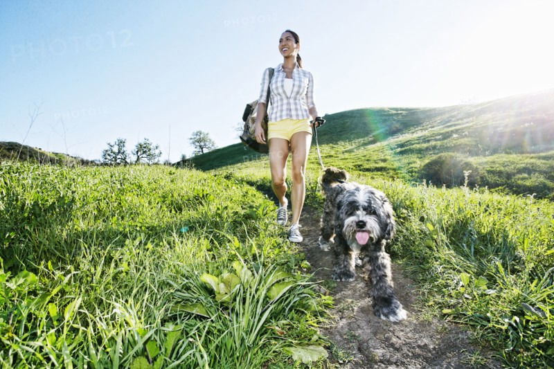 Mixed race woman walking dog on grassy hillside